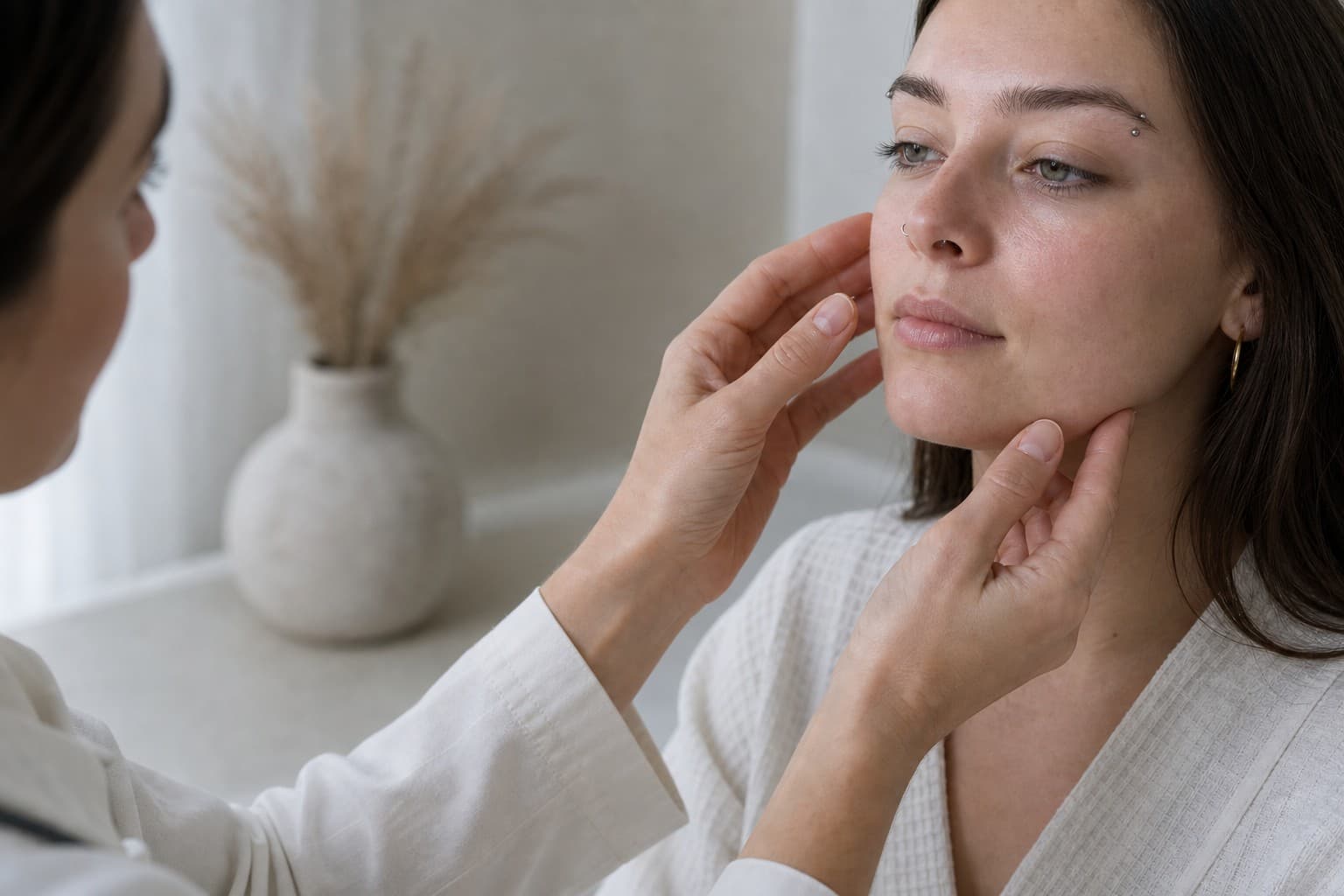 Practitioner’s hands gently assessing a patient’s cheek before treatment