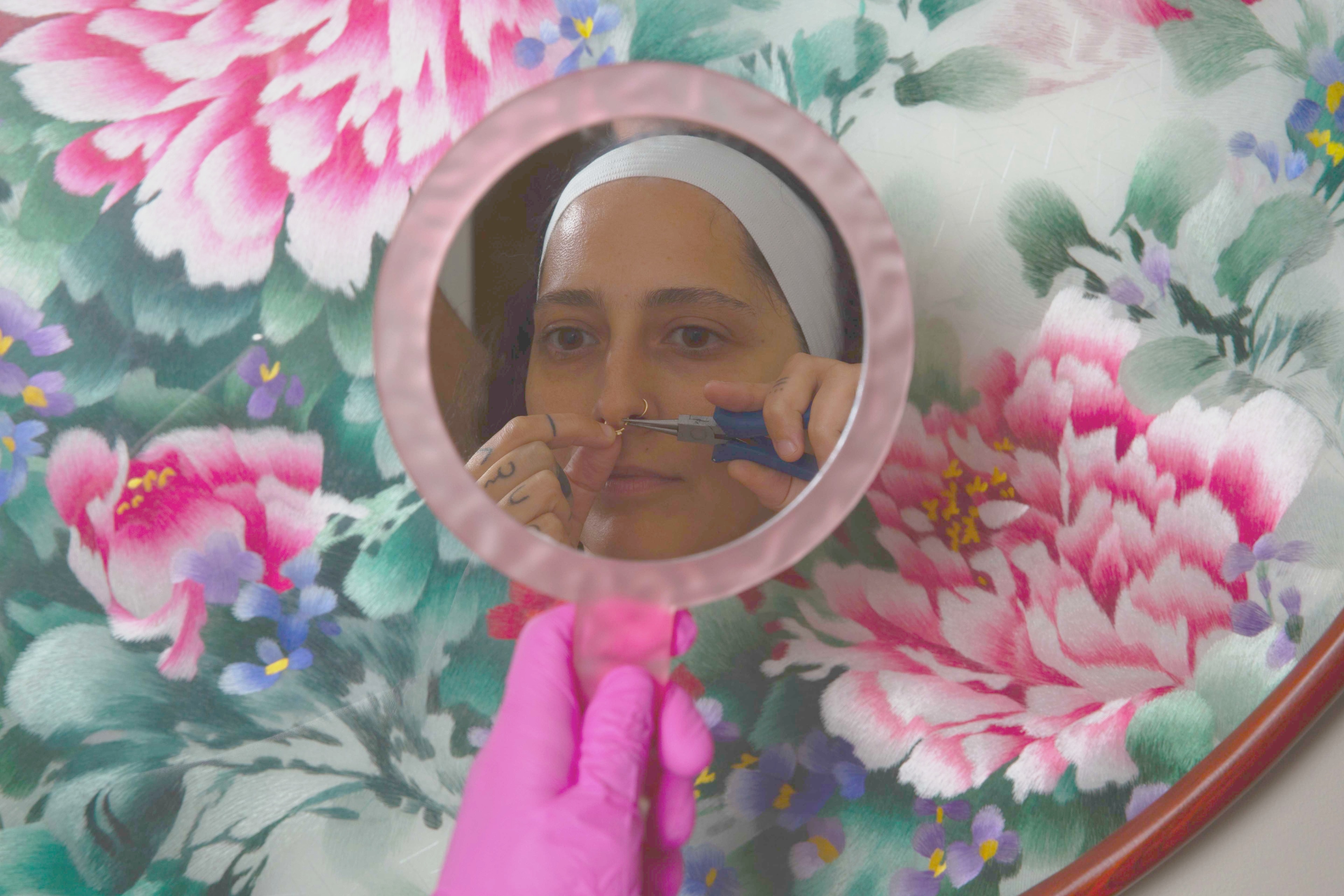 Client changing facial piercings in a hand mirror after clinical care